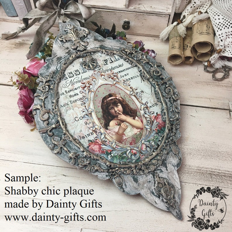 Pode incluir: Uma placa de madeira branca desgastada com uma moldura decorativa ornamentada. A placa apresenta um an&uacute;ncio vintage com uma menina em um vestido rosa e o texto "FIL Nombreus comhendes SERRATIO JURY ARSEILL UX EXPOSITE HORS C AUX EXPOSIC Da Co 9,1 JSINES AUX".