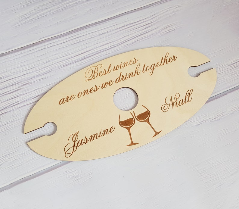 May include: Wooden wine holder with two slots for glasses. It has the text "Best wines are ones we drink together" and the names "Jasmine" and "Niall" engraved on it.