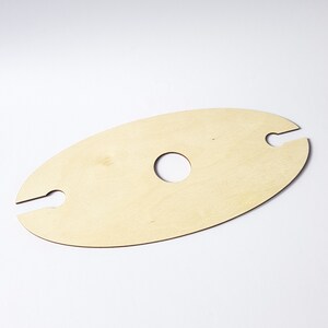 May include: A wooden wine bottle holder with two cutouts for holding bottles and a circular cutout in the center. The holder is light brown and oval shaped.