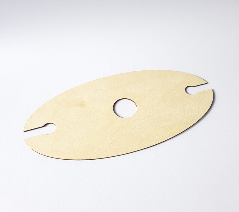 May include: A wooden wine bottle holder with two cutouts for holding bottles and a circular cutout in the center. The holder is light brown and oval shaped.