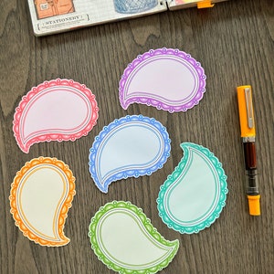 May include: Six colorful paisley-shaped paper stickers with scalloped edges. The stickers are blank and can be used for notes, reminders, or journaling.