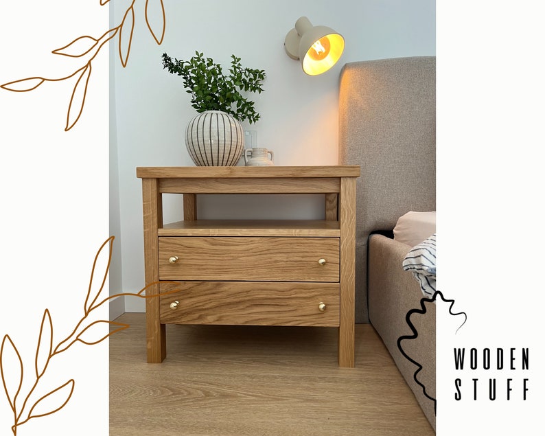 May include: A light oak nightstand featuring two drawers with small round gold-toned knobs and an open shelf space below the top surface. The wood grain is visible throughout the structure, which stands on four sturdy legs. Text reads WOODEN STUFF.