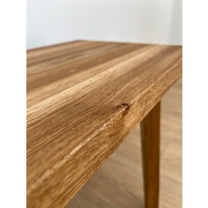 May include: Close-up of a wooden table with a natural wood grain finish. The table has a light brown color and a rectangular top. The legs are a similar color and are slightly tapered. The table is likely for indoor use.