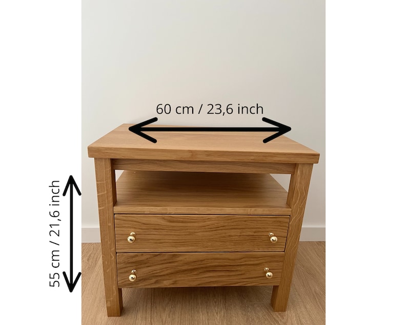 May include: A light brown wooden nightstand with an open shelf and two drawers featuring gold-toned knobs. The nightstand measures 23.6 inches in width and 21.6 inches in height, as indicated by the black arrows and text printed on the image.