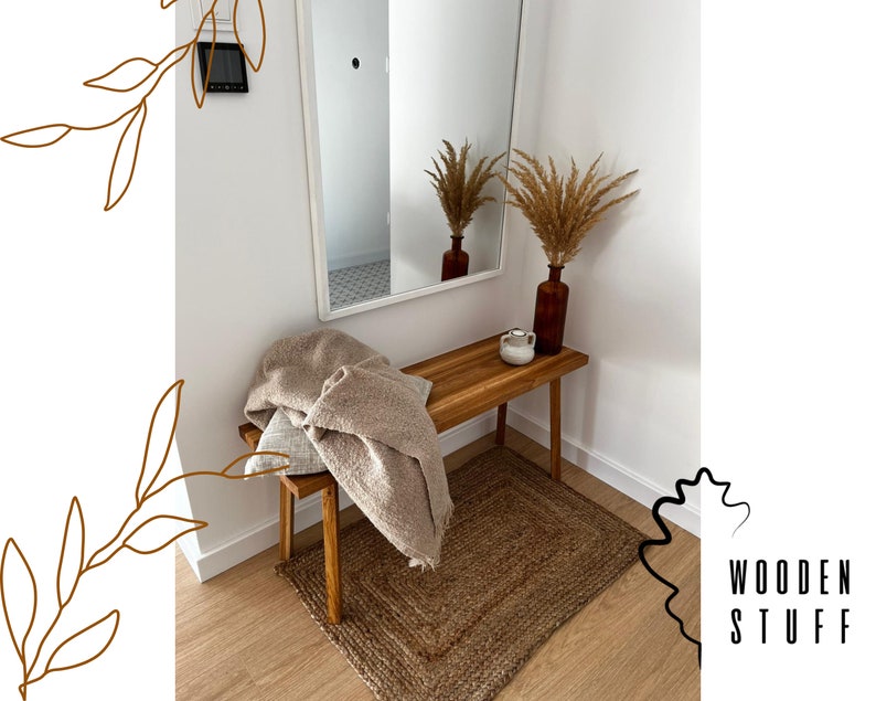May include: A wooden bench with a rectangular jute rug and a brown vase with dried plants. A beige throw blanket and a pillow are on the bench. The wall is white with a mirror and the text "WOODEN STUFF".