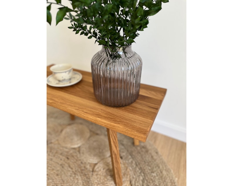 May include: A translucent, smoky grey glass vase with a vertical ribbed texture. The vase has a wide, rounded body and a narrow neck, containing a cluster of dark green leafy branches. The glass reflects light along its ridges.