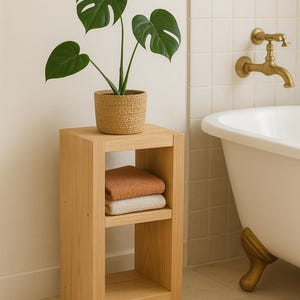 Peut inclure: Étagère en bois clair à trois niveaux avec un panier tressé contenant une plante en pot. Deux serviettes pliées, orange et crème, sont sur l'étagère du milieu. La scène se déroule dans une salle de bain avec une baignoire blanche et des accessoires dorés.