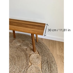 May include: A rectangular wooden bench with a natural brown grain finish and four straight legs. The bench features a clear measurement indicator on the right side, showing a width of 11.81 inches, providing a clear sense of scale for the furniture piece.