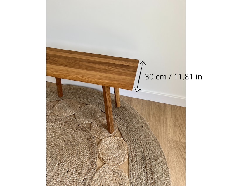 May include: A rectangular wooden bench with a natural brown grain finish and four straight legs. The bench features a clear measurement indicator on the right side, showing a width of 11.81 inches, providing a clear sense of scale for the furniture piece.