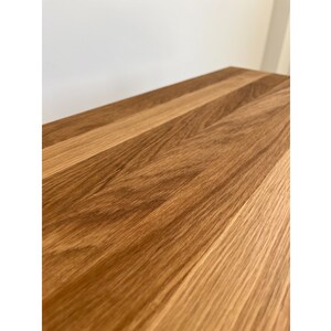May include: A rectangular wooden surface featuring a natural light brown grain pattern. The wood planks are joined together, displaying a smooth finish with visible organic textures and varying shades of tan and medium brown throughout the surface.