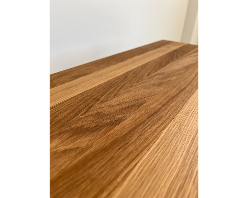 May include: A rectangular wooden surface featuring a natural light brown grain pattern. The wood planks are joined together, displaying a smooth finish with visible organic textures and varying shades of tan and medium brown throughout the surface.