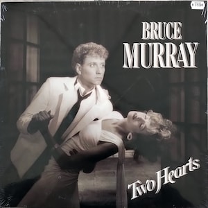 May include: A black and white album cover featuring Bruce Murray. The album cover shows a man in a white suit holding a woman in a white dress. The album title is "Two Hearts".