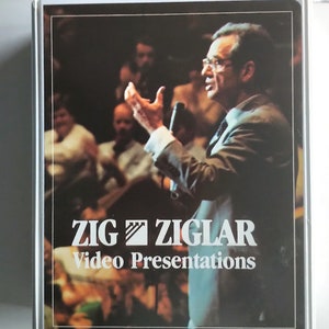Puede incluir: Una imagen en blanco y negro de un hombre hablando a una multitud. El hombre lleva traje y corbata. La imagen tiene el texto "ZIG ZIGLAR Video Presentations" en la parte inferior.