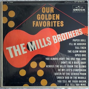 Peut inclure: Une pochette d'album vinyle noir et rouge avec une guitare rouge et le texte "THE MILLS BROTHERS" en blanc. Le titre de l'album est "OUR GOLDEN FAVORITES" et le label est "DECCA RECORDS". L'album comprend des chansons telles que "Paper Doll", "I'll Be Around", "Till Then", "The Glow Worm", "Opus One", "You Always Hurt The One You Love", "Don't Be A Baby, Baby", "Across The Alley From The Alamo", "Be My Life's Companion", "Queen Of The Senior Prom", "Smack Dab In The Middle", "You Tell Me Your Dream, I'll Tell You Mine".