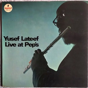 Puede incluir: Una portada de álbum en blanco y negro con la silueta de un hombre tocando la flauta. El título del álbum es "Yusef Lateef Live at Pep's" y la discográfica es "Impulse!"
