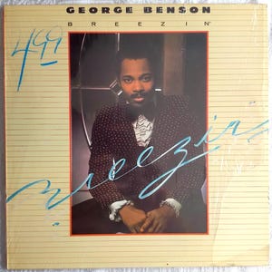 May include: Album cover for George Benson's "Breezin'" featuring a portrait of Benson in a patterned suit and bow tie. The album title and artist's name are at the top. The word "Breezin'" is written in a cursive font across the image, with a price written in blue.