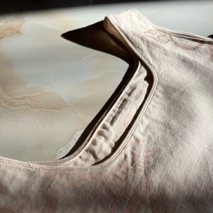 May include: A light beige sleeveless top with a delicate floral pattern. The top is made of a soft, textured fabric.