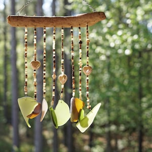 Peut inclure: Un carillon en bois avec plusieurs fils de perles et de morceaux de verre suspendus. Les perles sont brunes, blanches et beiges. Les morceaux de verre sont verts et bruns. Le carillon est suspendu à une branche dans une forêt.