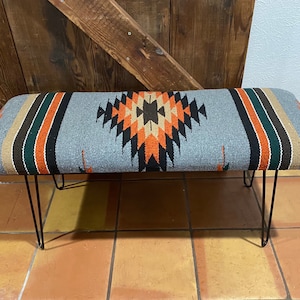 May include: A gray bench with a black metal frame and a colorful woven seat cushion with geometric patterns in orange, brown, and green.