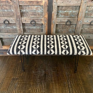 Puede incluir: Un banco con estampado en blanco y negro con un asiento de tejido tejido y patas de horquilla negras.