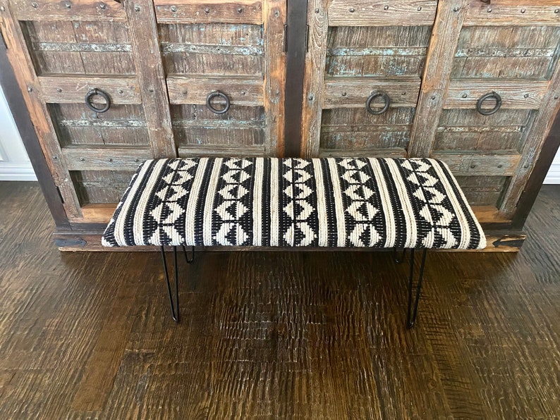 Puede incluir: Un banco con estampado en blanco y negro con un asiento de tejido tejido y patas de horquilla negras.