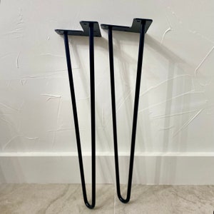 K&ouml;nnte beinhalten: Zwei schwarze Haarnadel-Tischbeine. Jedes Bein hat eine flache Montageplatte mit vorgebohrten L&ouml;chern und ein schlankes, gebogenes Design. Die Beine sind aus Metall und f&uuml;r M&ouml;belprojekte geeignet.