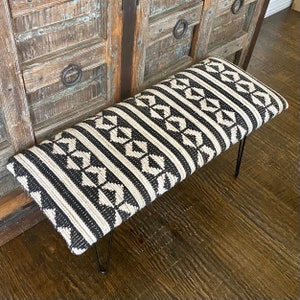 Puede incluir: Un banco con estampado en blanco y negro con un asiento de tejido tejido y patas de horquilla negras.
