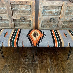 May include: A gray bench with a black, orange, and green geometric pattern. The bench has black hairpin legs.