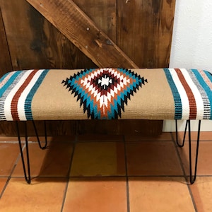 May include: A tan and blue patterned bench with black hairpin legs. The bench has a geometric design with stripes and a diamond shape in the center.