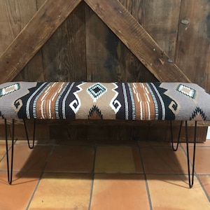 May include: A brown, black, and white patterned bench with black hairpin legs. The bench is made of a woven fabric and is sitting on a tiled floor.