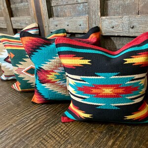 May include: Four decorative throw pillows with a southwestern geometric pattern in shades of black, turquoise, red, yellow, and white.
