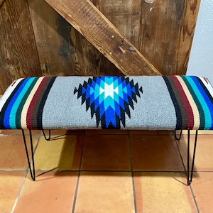 May include: A gray bench with black metal hairpin legs. The bench is covered in a colorful woven fabric with a geometric pattern in shades of blue, turquoise, white, and black.