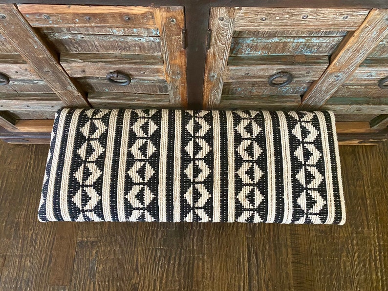 Puede incluir: Coj&iacute;n de banco estampado en blanco y negro con un dise&ntilde;o geom&eacute;trico. El coj&iacute;n est&aacute; hecho de tejido tejido y tiene una forma rectangular.