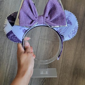May include: Purple and silver Minnie Mouse ears with a sparkly bow and a patterned design featuring a butterfly and the text "Stay True".