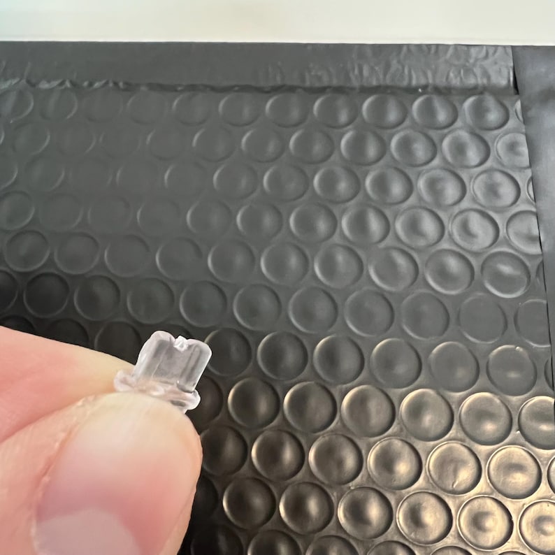May include: A clear plastic piece with a small hole in the center. It is a replacement part for a product.