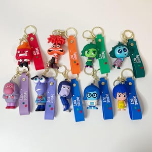 May include: Set of 10 Inside Out character keychains. Each keychain features a different character from the movie, including Joy, Sadness, Anger, Fear, and Disgust. The keychains are made of plastic and have a metal ring for attaching to keys or bags.