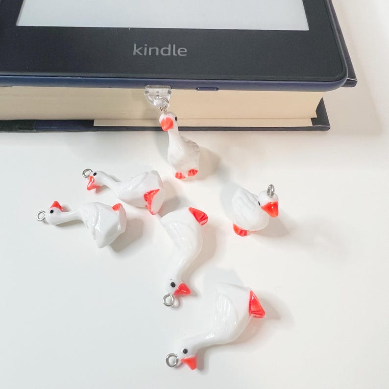 May include: Six white ceramic goose charms with red beaks and silver loops. The charms are scattered on a white surface.