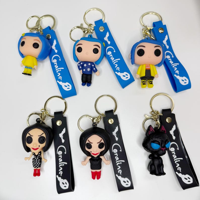 May include: A selection of keyrings featuring characters from the film "Coraline." The keyrings showcase various character designs, including a girl with blue hair, a woman in a black dress, and a black cat. Each keyring has a strap that says "Coraline."