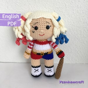 Puede incluir: Muñeca amigurumi de crochet de Harley Quinn, un personaje del universo DC Comics. La muñeca lleva un traje rojo y azul con un cinturón negro y zapatos blancos. Está sosteniendo un bate de béisbol marrón. La muñeca mide aproximadamente 25 cm de alto.