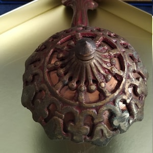 May include: A decorative, ornate, gold and red metal incense burner with a detailed design. The burner has a round base and a long, ornate handle.