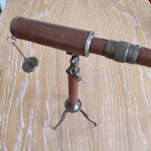 May include: A vintage brass telescope with a brown leather covering on the barrel, mounted on a tripod stand with adjustable legs.