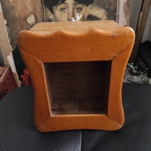 May include: A wooden box with a glass front and a decorative, wavy top edge. The box is made of light brown wood and has a natural finish.