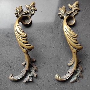 以下が含まれることがあります： 複雑な花柄が施された、金色の装飾的なドアノブが2つ。ノブには装飾的なスクロールワークパターンと、わずかに盛り上がった丸い中心部があります。