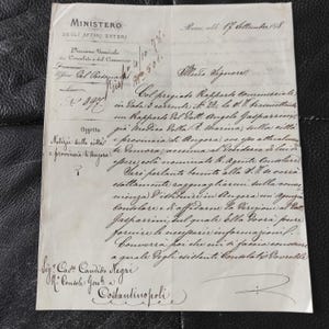 May include: A vintage document with handwritten text in Italian. The paper is aged, with visible creases and stains. The document includes the words "Ministero degli Affari Esteri" and a signature at the bottom. The text is in black ink.
