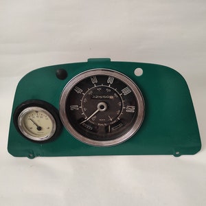 May include: A green dashboard with a round speedometer and a smaller round gauge. The speedometer has a black face with white numbers and a silver needle. The gauge has a white face with black numbers and a silver needle. The speedometer reads up to 120 mph and the gauge reads up to 100 degrees.