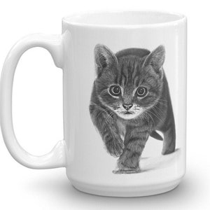 May include: A white ceramic mug with a black and white drawing of a kitten looking at the camera. The kitten is walking towards the viewer.