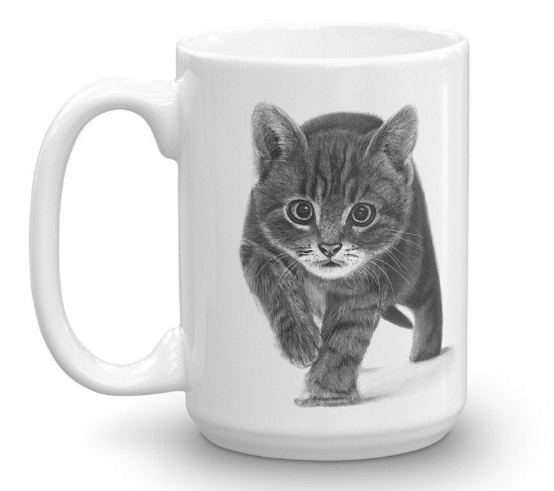 May include: A white ceramic mug with a black and white drawing of a kitten looking at the camera. The kitten is walking towards the viewer.