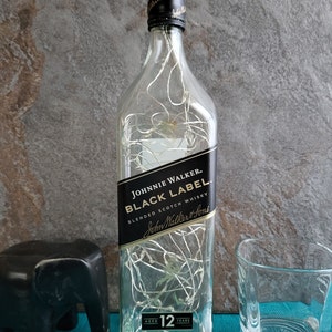 Puede incluir: Una botella de vidrio transparente con una etiqueta negra que dice "JOHNNIE WALKER. BLACK LABEL BLENDED SCOTCH WHISKY John Walker & Sons AGED 12 YEARS". La botella est&aacute; llena de luces blancas.