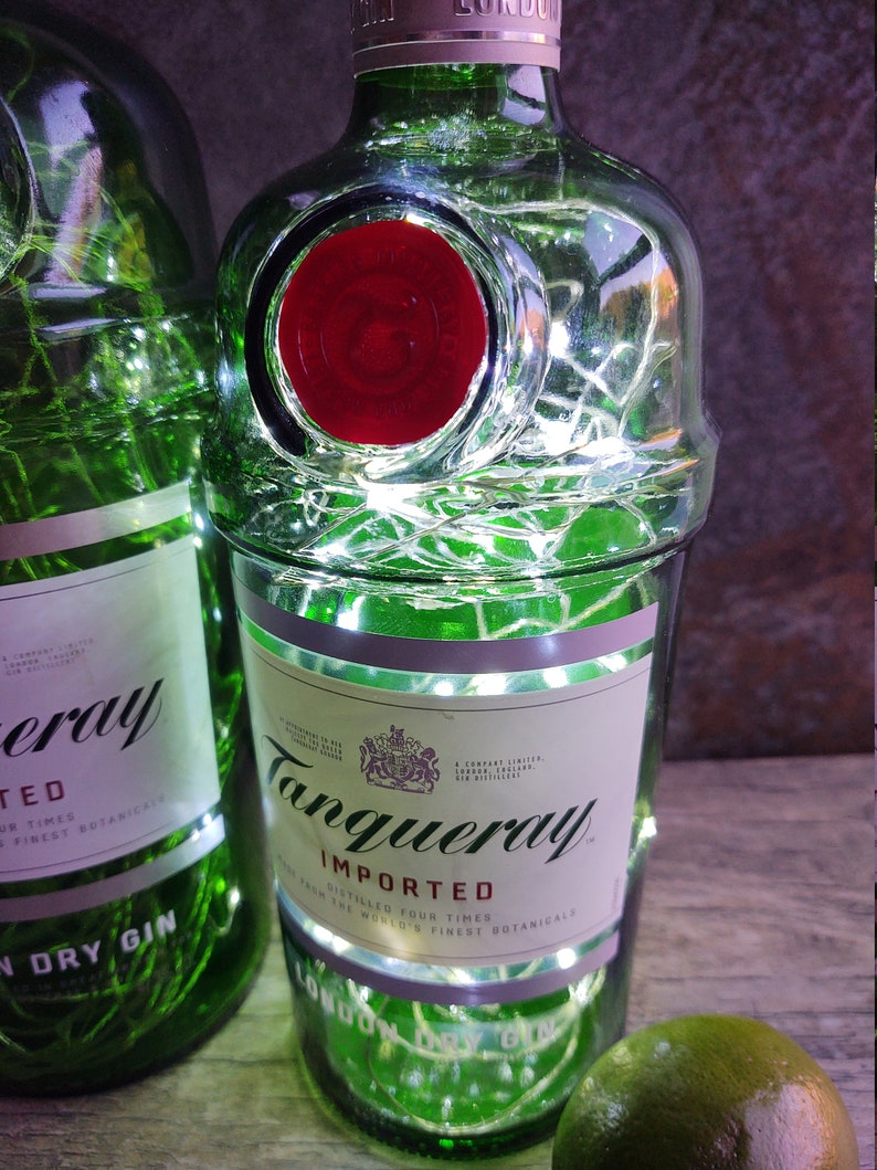 May include: A green glass bottle with a red label and white lights wrapped around it. The label says "Tanqueray Imported" and "Distilled Four Times from the World's Finest Botanicals".