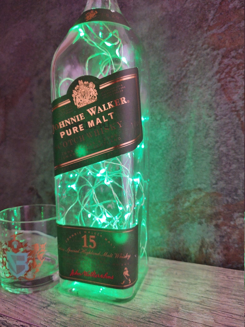 May include: A green glass bottle with a label that reads "Johnnie Walker, Pure Malt Scotch Whisky" and "15 Special Highland Malt Whisky". The bottle is decorated with green fairy lights.
